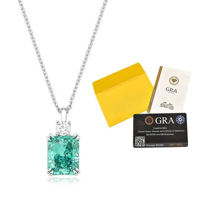 Colar com pedra verde retangular e pequena pedra branca em garras, ao lado de envelope amarelo e cartão GRA