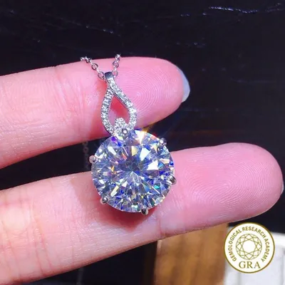Pingente com grande pedra redonda de moissanite em garras e alça em gota cravejada, segurado entre os dedos