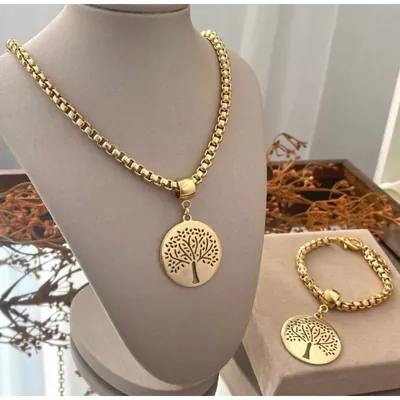 Colar dourado de corrente grossa com medalha vazada de árvore em busto cinza e pulseira igual sobre caixa bege