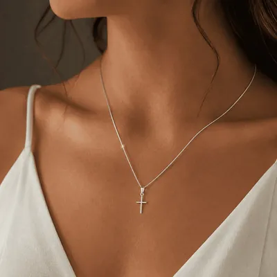 Colar de corrente fina prateada com pequena cruz de hastes finas, usado sobre blusa branca de decote em V