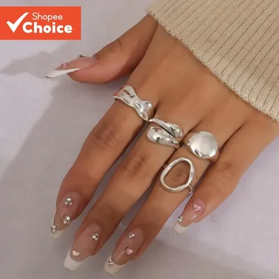 Mão feminina com quatro anéis prateados de formas onduladas, gotas, placa redonda e oval vazado, unhas francesinhas