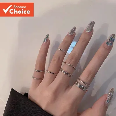 Mão com unhas cromadas usando vários anéis prateados finos, um anel de elos e uma faixa larga, em dedos diferentes
