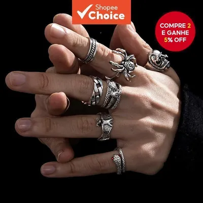 Mão masculina usando vários anéis prateados envelhecidos: caveira, aranha, cobras, corrente e asas