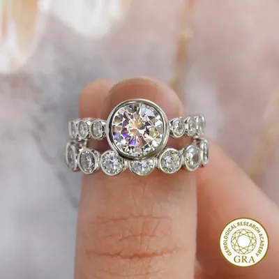 Dois anéis prateados empilhados no dedo, um com moissanite redonda grande e outro com pedras redondas em moldura