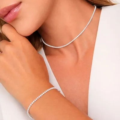 Mulher de blusa branca usando choker e pulseira prateadas com fileira de pequenas pedras brilhantes