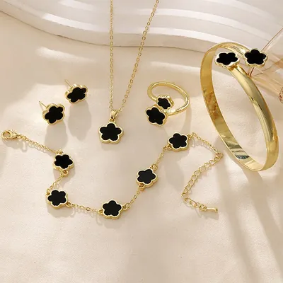 Colar, brincos, anel, pulseira de corrente e bracelete dourados com flores pretas de cinco pétalas sobre tecido creme