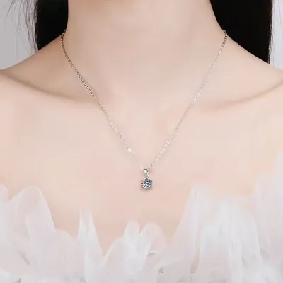 Colar de corrente fina prateada com pequena pedra redonda de moissanite no pescoço, sobre blusa de tule branco