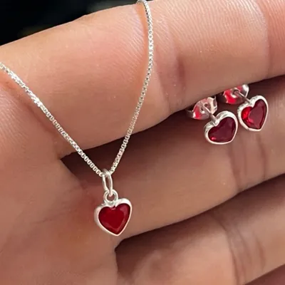 Colar de corrente veneziana com pingente de coração vermelho e par de brincos iguais apoiados sobre a mão