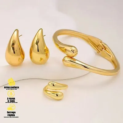 Brincos dourados em gota, bracelete com pontas cruzadas em gota e anel aberto, sobre fundo bege claro