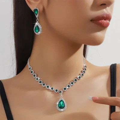 Modelo usando colar prateado com strass e pedras verdes redondas, pingente em gota verde e brinco em gota combinando