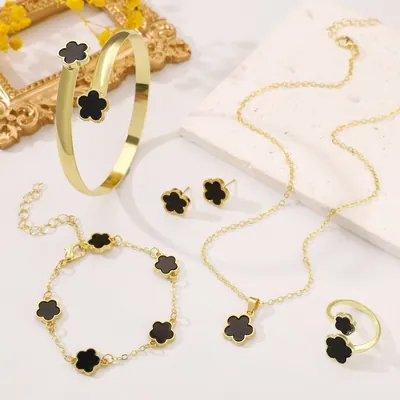 Bracelete, pulseira, colar, brincos e anel dourados com flores pretas de cinco pétalas sobre fundo claro com pedra e moldura