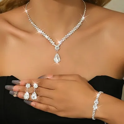 Mulher de tomara que caia preto usando colar em V com gota de pedras claras, brincos de gota na mão e pulseira de strass