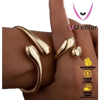 Pulso com bracelete dourado aberto de pontas em gota e dedo com anel aberto no mesmo formato, acabamento espelhado