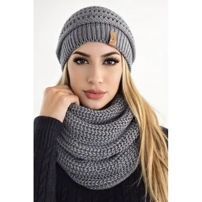 Mulher usando touca cinza de tricô com ponto vazado e etiqueta marrom, e gola cachecol cinza de tricô grosso no pescoço