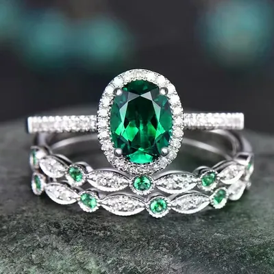 Três anéis prateados empilhados: um com pedra verde oval e halo de pedrinhas, dois com pedrinhas verdes e brancas