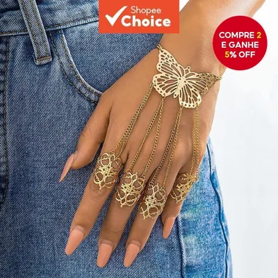 Mão feminina sobre bolso de jeans com corrente dourada, borboleta vazada no dorso e anéis rendados em quatro dedos