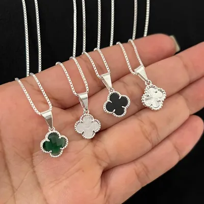 Quatro correntes prateadas com pingentes de trevo verde, branco, preto e prateado texturizado na palma da mão