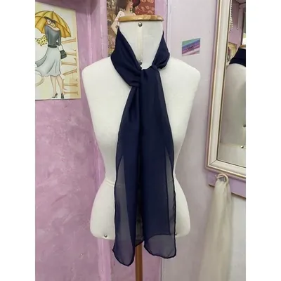 Echarpe azul-marinho de chiffon amarrada com nó solto no pescoço de um manequim branco, em ateliê de parede rosa