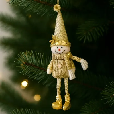 Boneco de neve de tecido dourado com gorro cônico, cachecol de franja branca e pernas finas, pendurado num galho de pinheiro