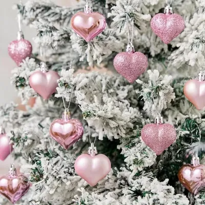 Enfeites de coração rosa, brilhantes, foscos e com glitter, pendurados numa árvore de Natal nevada