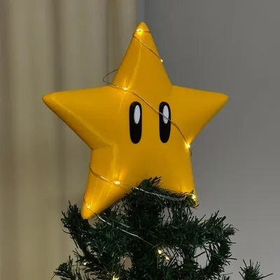 Estrela amarela com dois olhos pretos ovais no topo de árvore de Natal, enrolada num fio de luzinhas