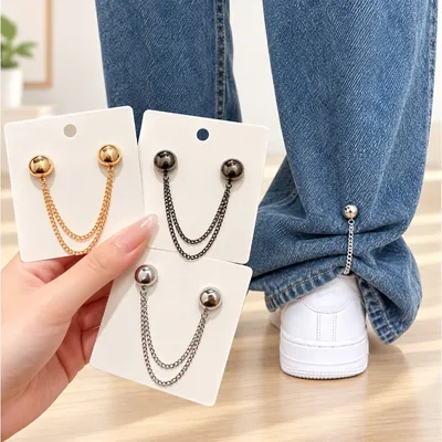 Três cartelas com botões dourados, grafite e prata ligados por corrente dupla e barra de calça jeans presa com a peça