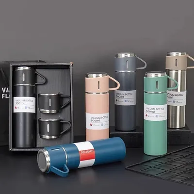 Garrafas térmicas de 500ml em preto, rosa, cinza, verde, bege e azul; a preta em caixa aberta com duas xícaras