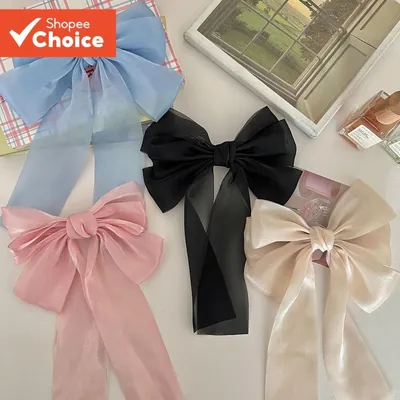 Quatro laços grandes de tecido translúcido com caudas longas nas cores azul-claro, preto, rosa e champanhe sobre mesa clara