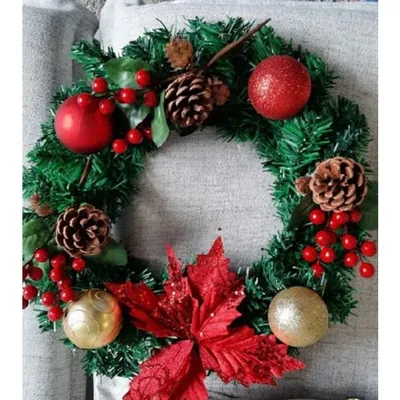 Guirlanda verde decorada com pinhas, frutinhas vermelhas, bolas com glitter e flor bico-de-papagaio, apoiada em sofá