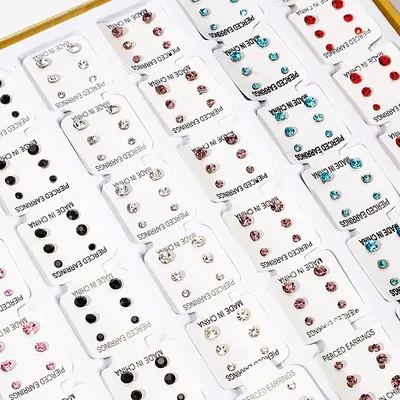 Bandeja com dezenas de cartelas brancas de brincos de strass em cristal, preto, rosa, vermelho e azul-piscina
