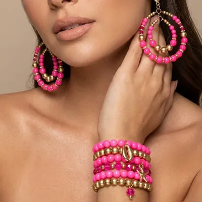 Modelo com brincos de argola dupla de contas pink e douradas e seis pulseiras empilhadas no pulso com pingentes
