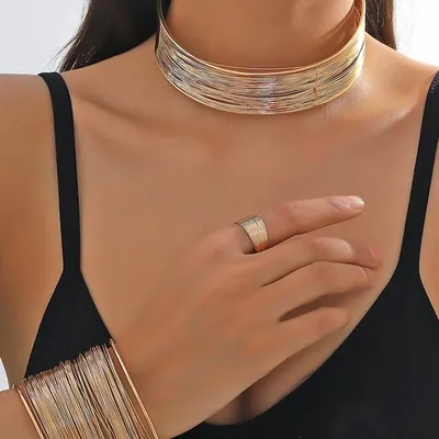 Mulher de blusa preta de alcinha usando choker larga de fios dourados, bracelete de fios no pulso e anel no indicador