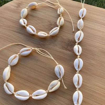 Choker e pulseiras de búzios brancos amarrados com cordão bege, sobre tábua de madeira com grama ao fundo