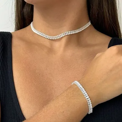 Mulher de blusa preta decote V usando colar curto e pulseira de zircônias baguete prateadas