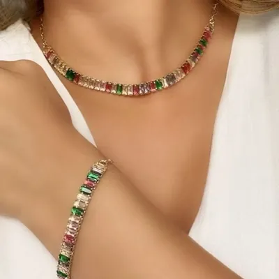 Mulher de blusa branca usando colar curto e pulseira dourados com zircônias baguete verdes, vermelhas, rosadas e claras