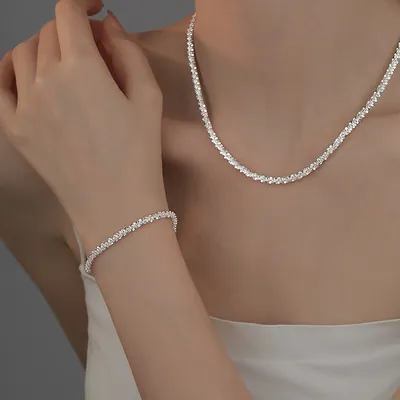 Mulher de blusa branca usando colar rente ao pescoço e pulseira fina, ambos de corrente prateada facetada e cintilante