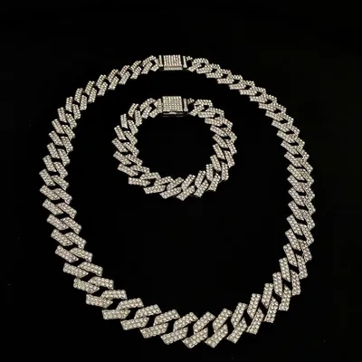 Corrente grossa e pulseira prateadas de elos cravejados com zircônias sobre fundo preto