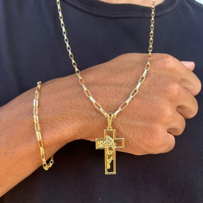 Homem de camiseta preta usando corrente tijolinho dourada com pingente de crucifixo vazado e pulseira combinando