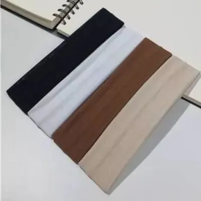 Quatro faixas de cabelo de tecido dobradas em preto, branco, marrom e bege ao lado de um caderno espiral