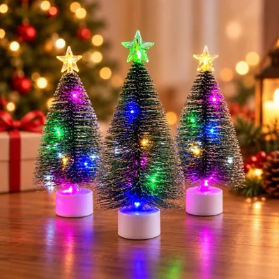 Três mini árvores de Natal de cerdas verdes com luzes coloridas, estrela no topo e base branca sobre mesa de madeira