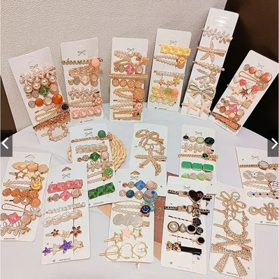 Várias cartelas de presilhas douradas com pérolas, laços, estrelas, corações e pedras coloridas sobre mesa branca