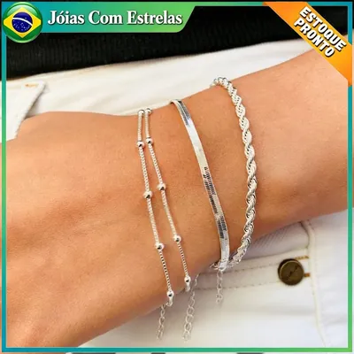 Pulso com três pulseiras prateadas: corrente de bolinhas em dois fios, fita lisa achatada e cordão torcido