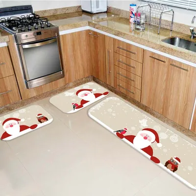 Três tapetes bege com Papai Noel, passarinho e coruja de gorro no chão de uma cozinha com armários de madeira