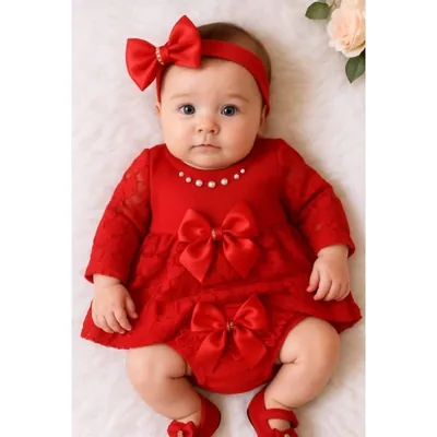Bebê deitada com vestido vermelho de renda e manga longa, pérolas no decote, laços de cetim, faixa de laço e sapatinhos