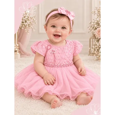 Bebê sentada sorrindo com vestido rosa de tule, cinto de pérolas, faixa de laço na cabeça e prendedor de chupeta de coração