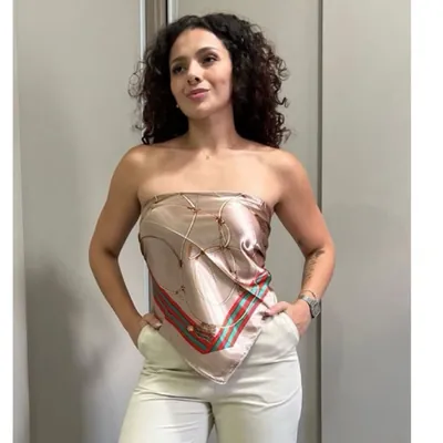 Mulher usando lenço de cetim bege com estampa de correntes douradas e listras vermelha e verde amarrado como top