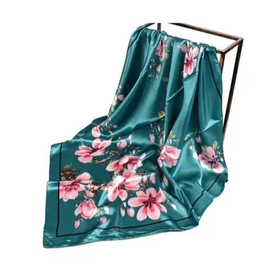 Lenço de cetim verde-petróleo com estampa de flores rosadas e galhos, com borda em linha escura, sobre suporte de metal