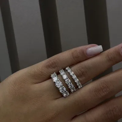 Mão com três meias alianças de pedras redondas claras empilhadas no dedo anelar, unhas claras