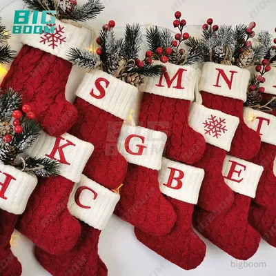 Meias de Natal de tricô vermelho com punho branco e letras bordadas em vermelho, penduradas com ramos de pinheiro