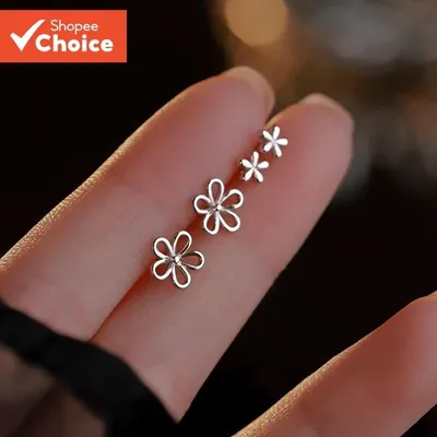 Mini brincos de flor prateados, dois vazados e dois menores de pétala cheia, apoiados sobre dedos
